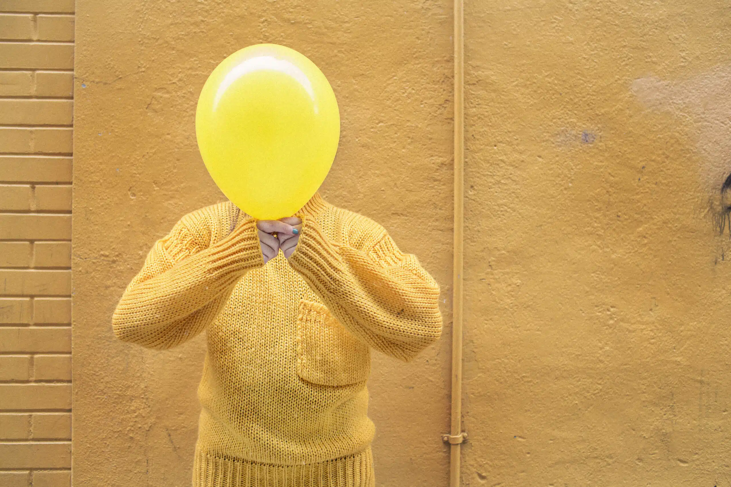 Person står foran væg; holder ballon foran hovedet, så ansigtet ikke kan ses.